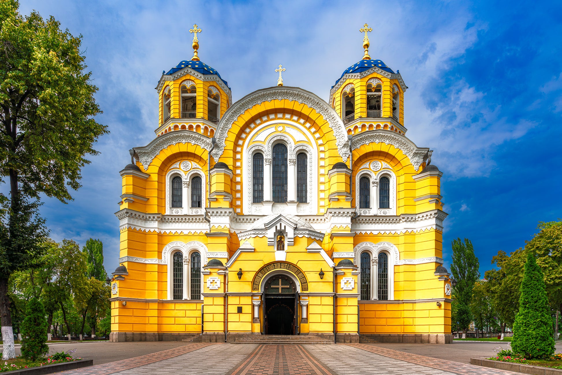 Colour photograph of Saint Volodymyr’s Cathedral in Kyiv with a bright yellow facade and blue domes beneath a clear sky