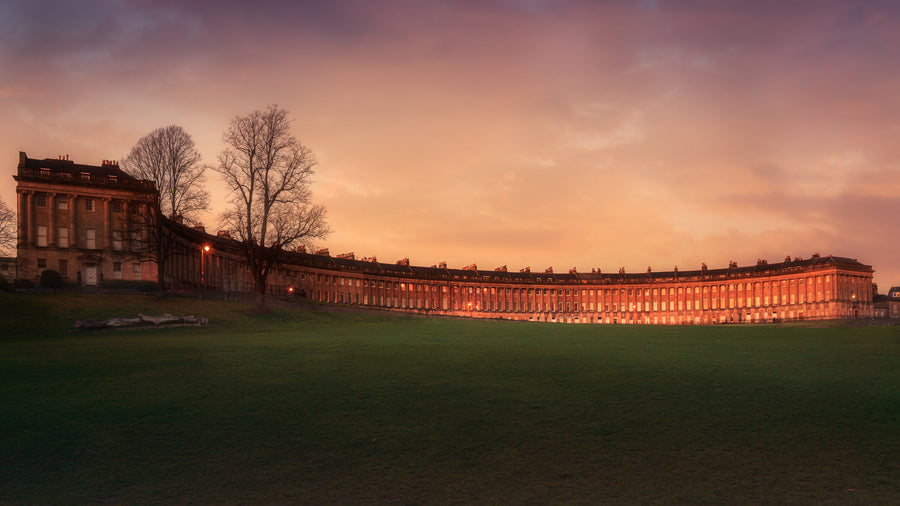 A fine art colour photograph of the Royal Crescent in Bath at sunset with warm light on the façade and a calm open lawn in the foreground.