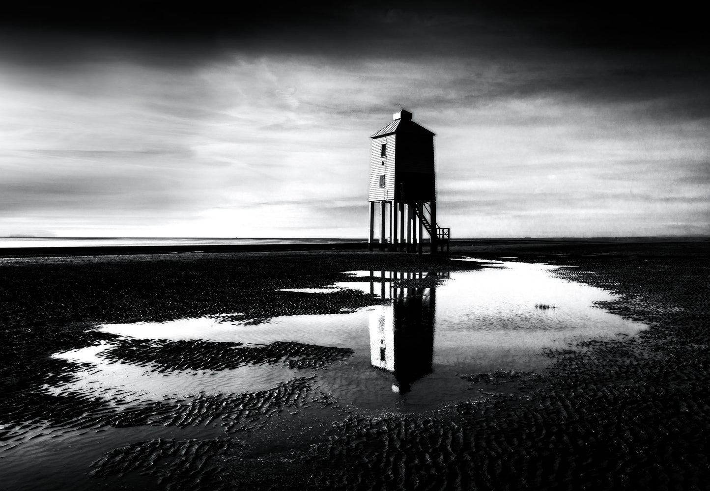 Black and white fine art photograph of Burnham-on-Sea Lighthouse on stilts, reflected in tidal pools at low tide, Somerset coast.
