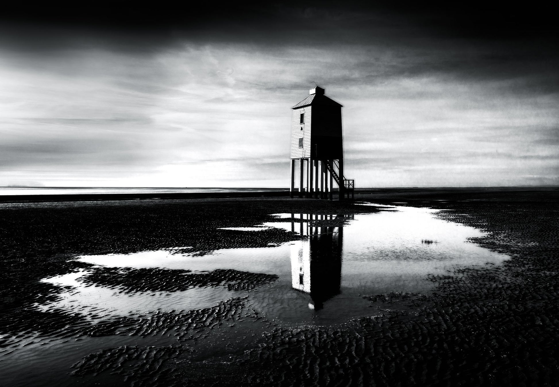 Black and white fine art photograph of Burnham-on-Sea Lighthouse on stilts, reflected in tidal pools at low tide, Somerset coast.