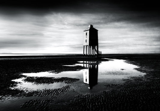 Black and white fine art photograph of Burnham-on-Sea Lighthouse on stilts, reflected in tidal pools at low tide, Somerset coast.
