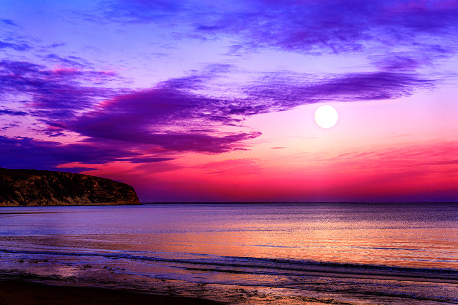 Moon rising over Swanage Bay at twilight with colourful sky reflecting on calm sea and gentle shoreline.