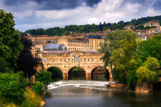 Fine art photo of Pulteney Bridge and the River Avon weir in Bath, surrounded by summer greenery and stormy skies