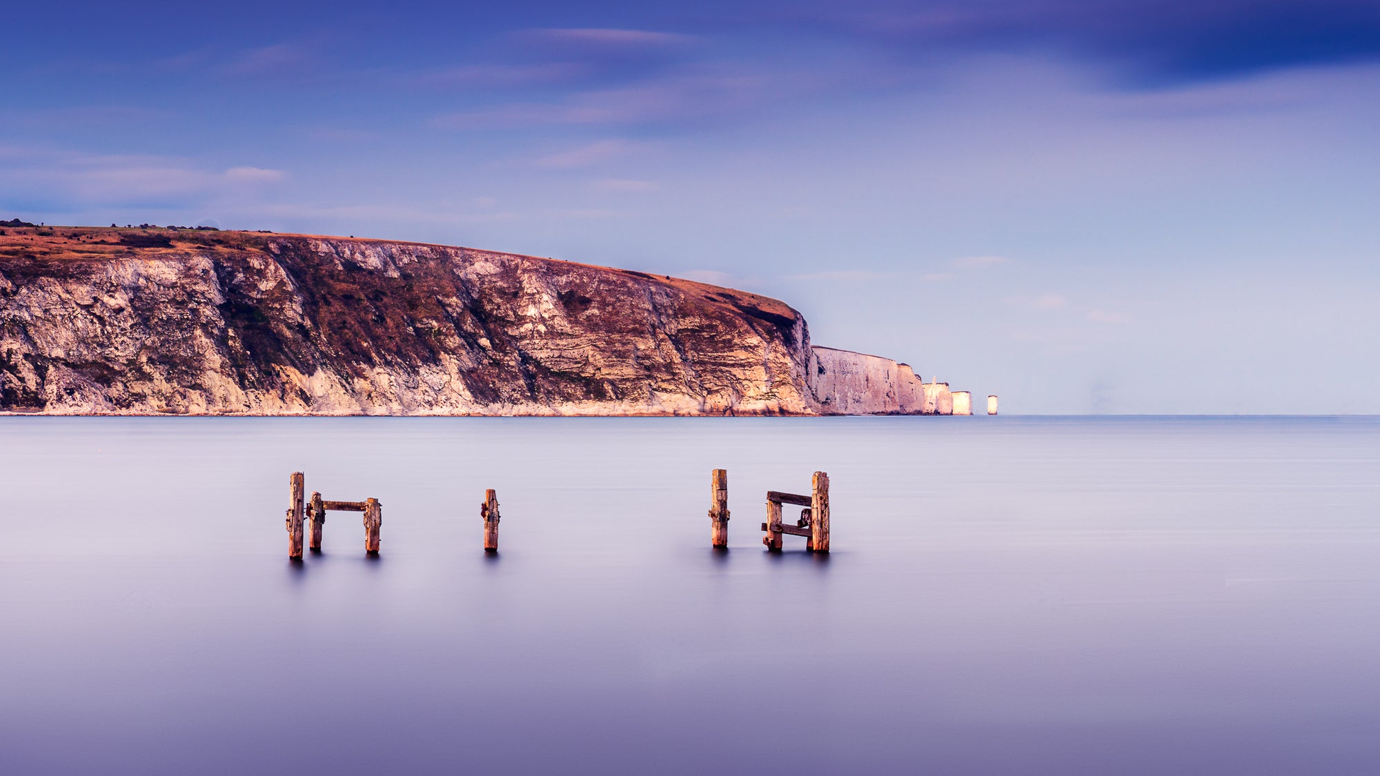 Long exposure photograph of old pier remains in Swanage Bay with smooth water and distant cliffs