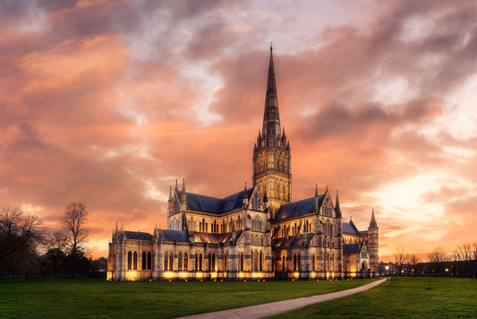Fine art photograph of Salisbury Cathedral at dusk with a warm sunset sky, golden floodlighting, and England’s tallest spire.