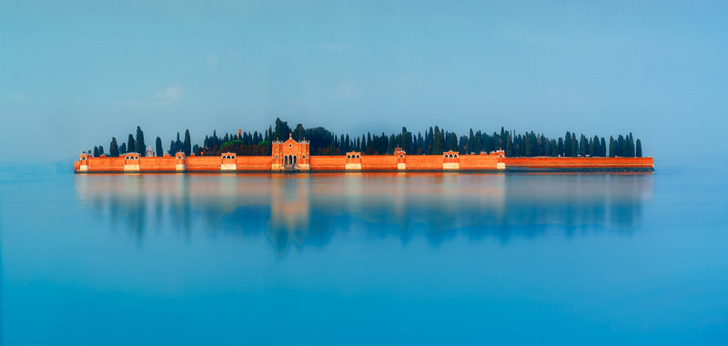 A fine art colour photograph of San Michele cemetery in Venice, captured as a minimalist long exposure with smooth blue water and warm terracotta walls.