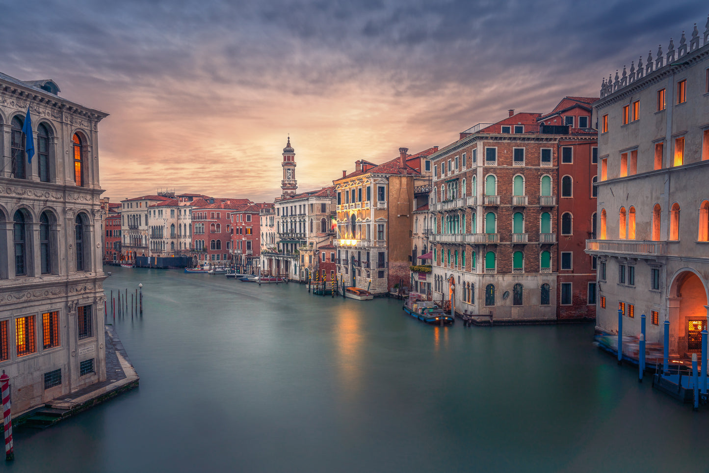 A fine art colour photograph of sunrise on the Grand Canal in Venice, with warm window light, calm long-exposure water, and historic buildings along the waterfront.