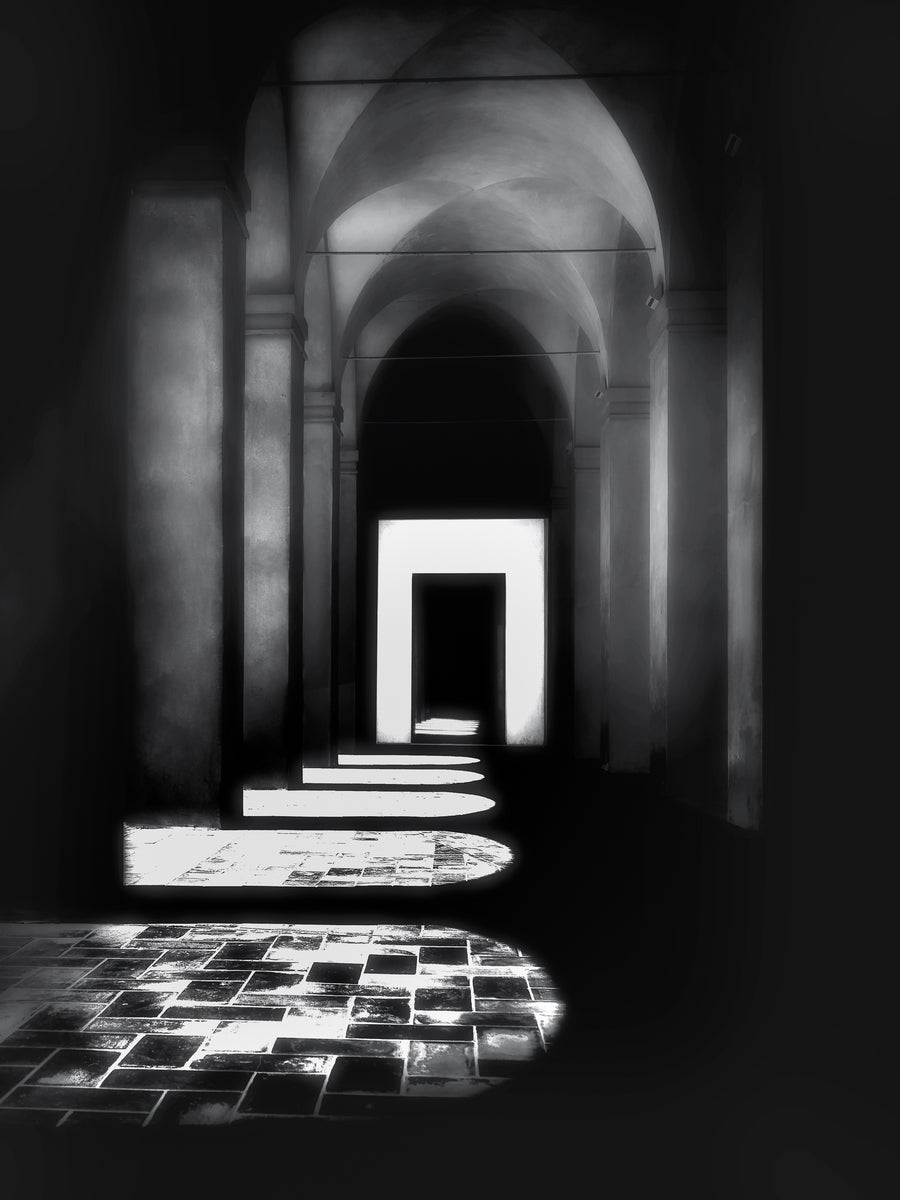 A fine art black and white photograph taken in the Real Alcázar of Seville, showing a sunlit colonnade with strong geometric shadows and historic stone arches.