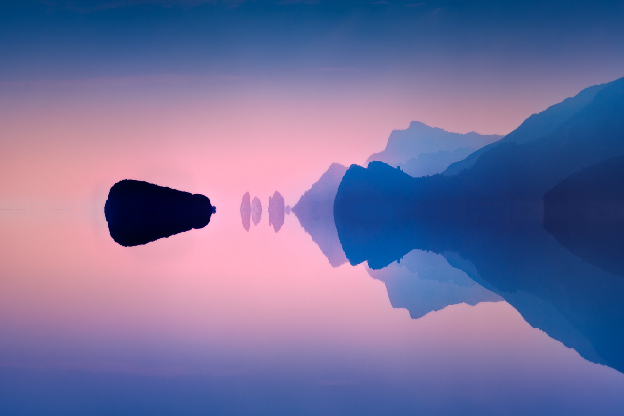 A fine art colour photograph of the Amalfi Coast at twilight showing calm mirrored water, soft pastel tones and minimalist silhouettes of cliffs and rocks.