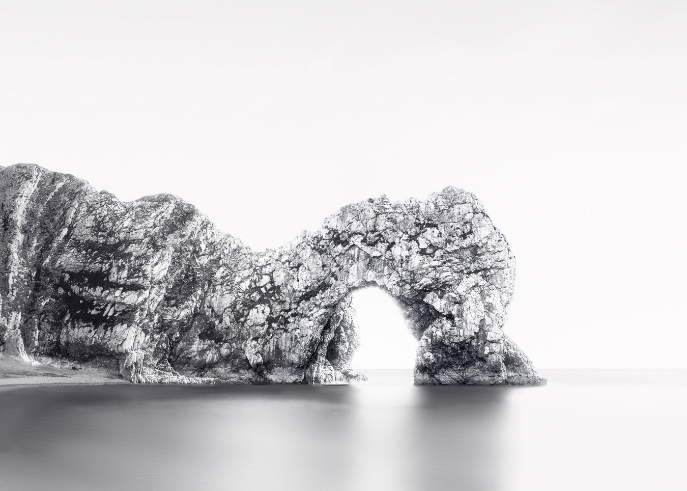 Minimalist black and white photograph of Durdle Door arch on the Jurassic Coast, with smooth sea and high-key sky. Fine art long exposure.