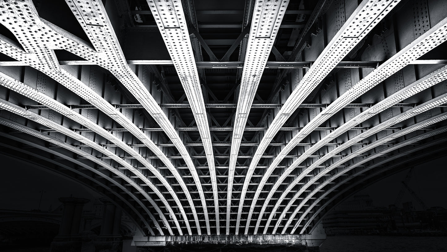 Black and white photograph of structural beams beneath a bridge in London showing symmetry and steel architecture