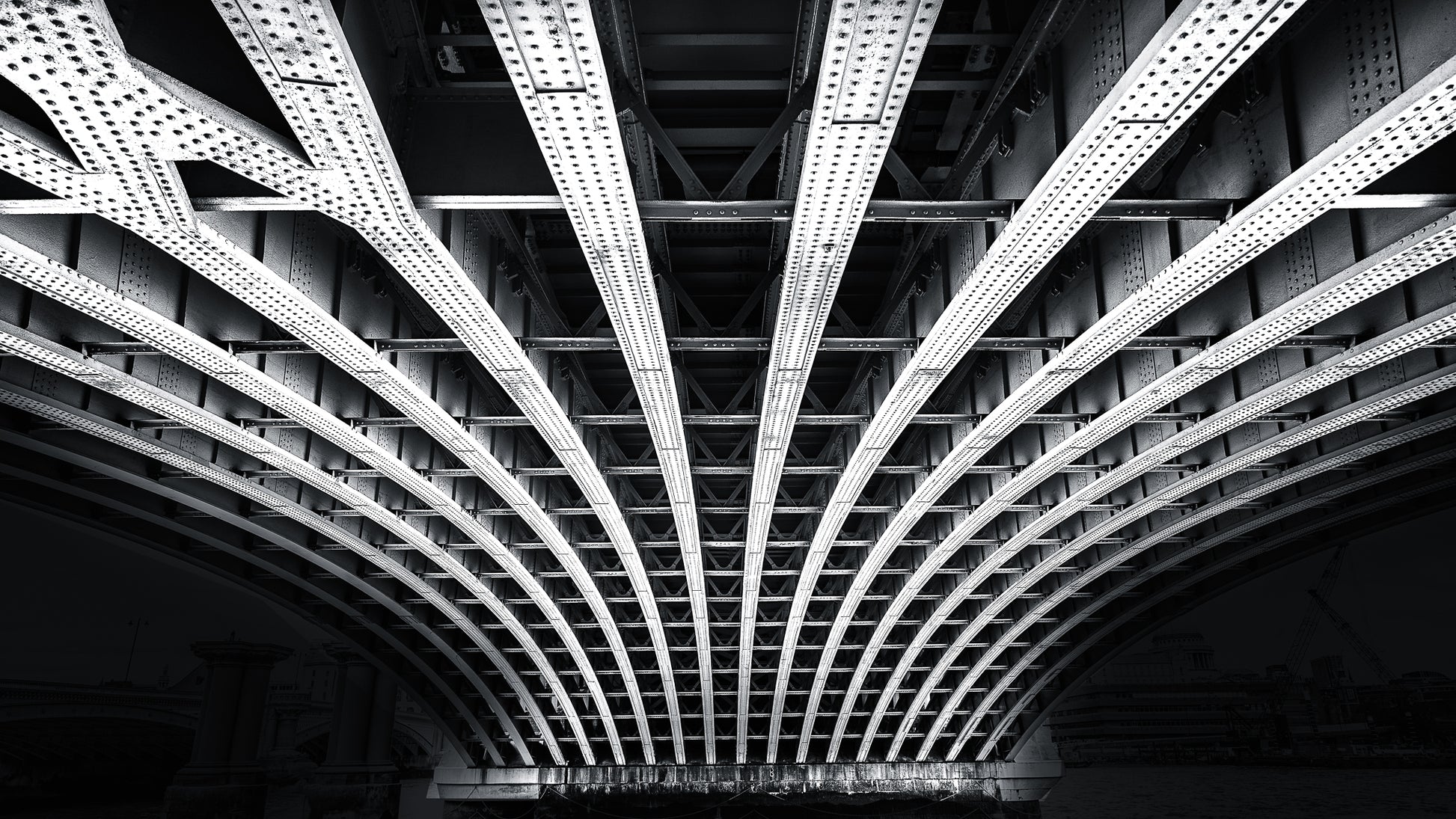 Black and white photograph of structural beams beneath a bridge in London showing symmetry and steel architecture