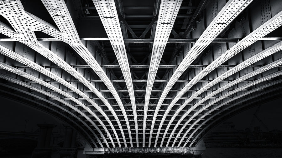 Black and white photograph of structural beams beneath a bridge in London showing symmetry and steel architecture
