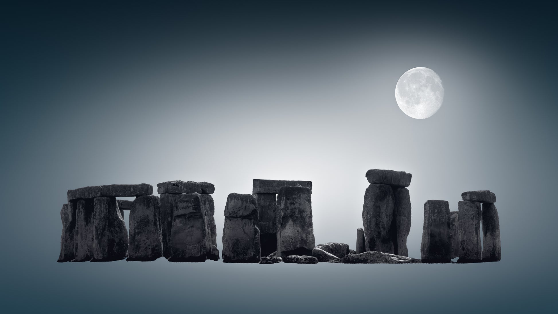 A fine art black and white photograph of Stonehenge in Wiltshire, England, with the full moon above the ancient stones at night.