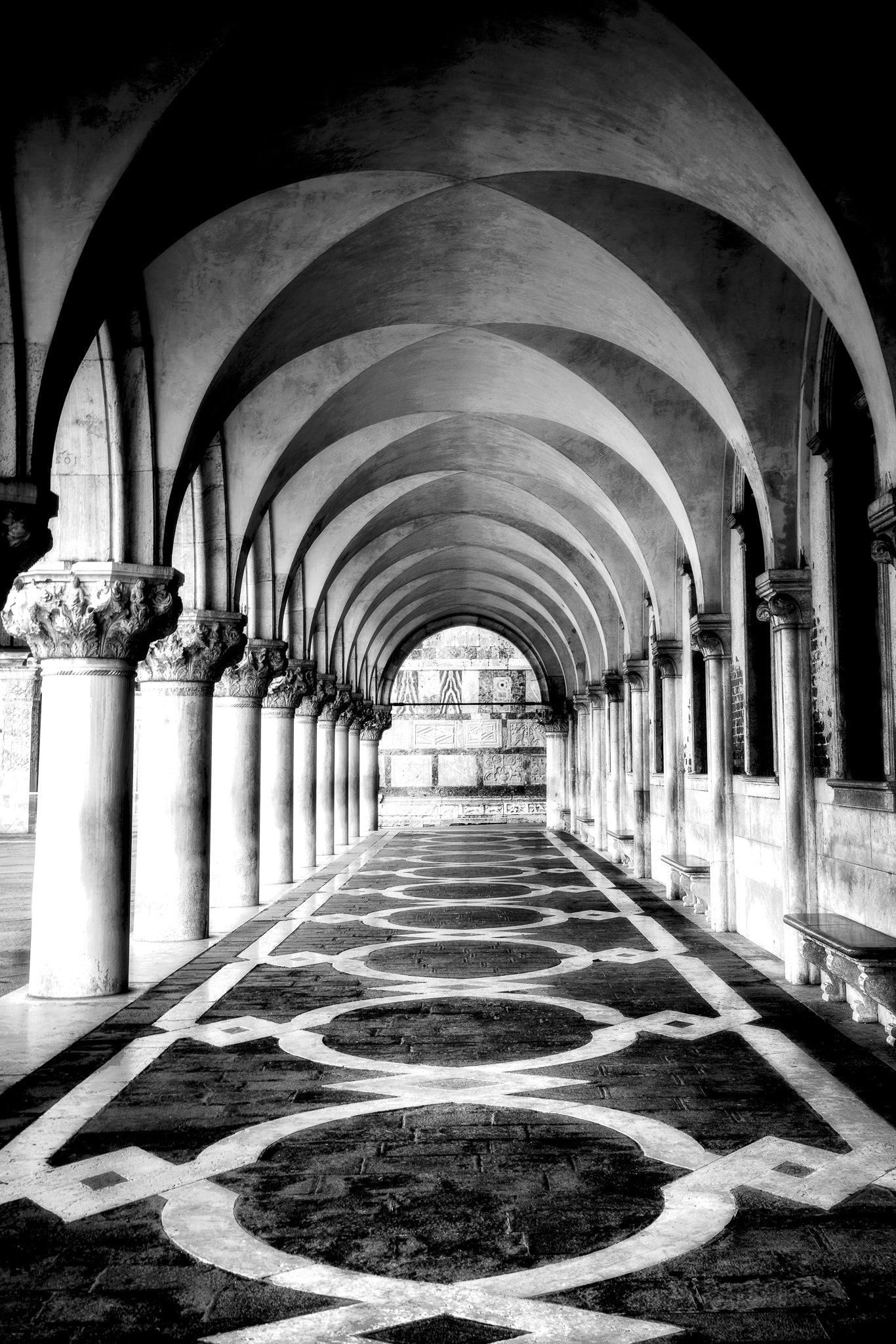 A fine art black and white photograph from Venice, Italy, showing the arched corridor of San Marco in soft early morning light.